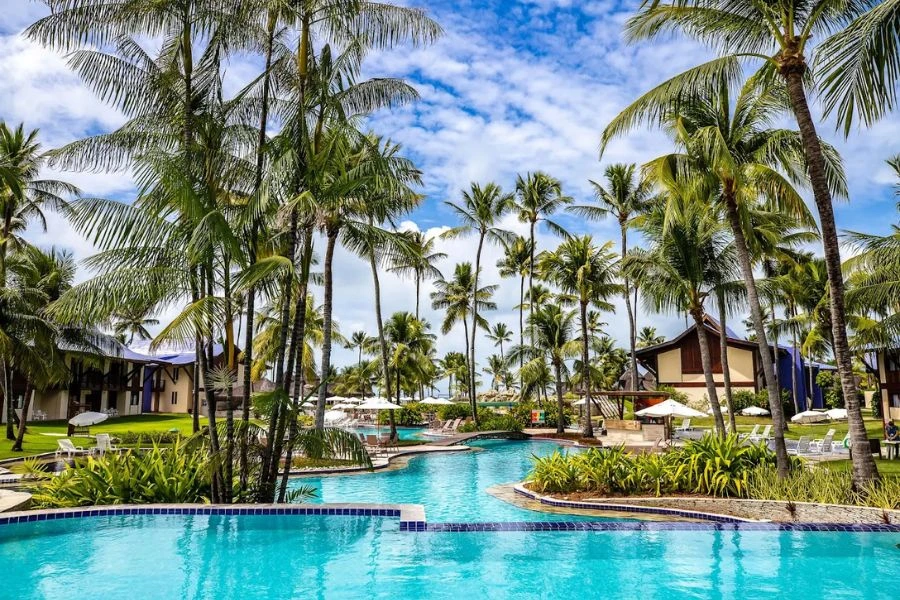 Area externa de um resort com piscina, palmeiras e céu azul limpo