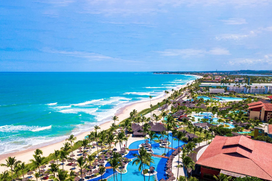 Vista aérea de resort à beira-mar com piscinas e coqueiros em Porto de Galinhas