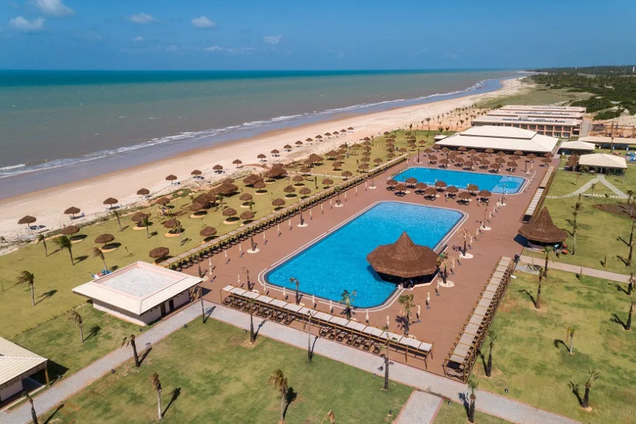 Vista aérea de resort à beira-mar com piscinas e espreguiçadeiras.