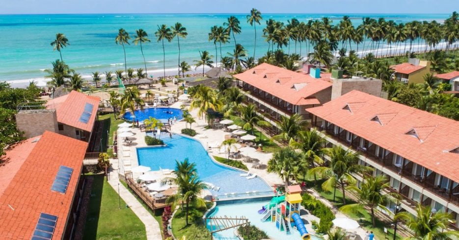 resort-beira-mar-com-palmeiras-ao-redor-Salinas-Maceió-All-Inclusive-Resort-Maceió-AL Imagem aérea de um resort à beira-mar, com palmeiras ao redor e uma grande piscina central. Ao fundo, a praia com águas cristalinas, enquanto no primeiro plano, um toboágua colorido e espreguiçadeiras oferecem conforto aos hóspedes.
